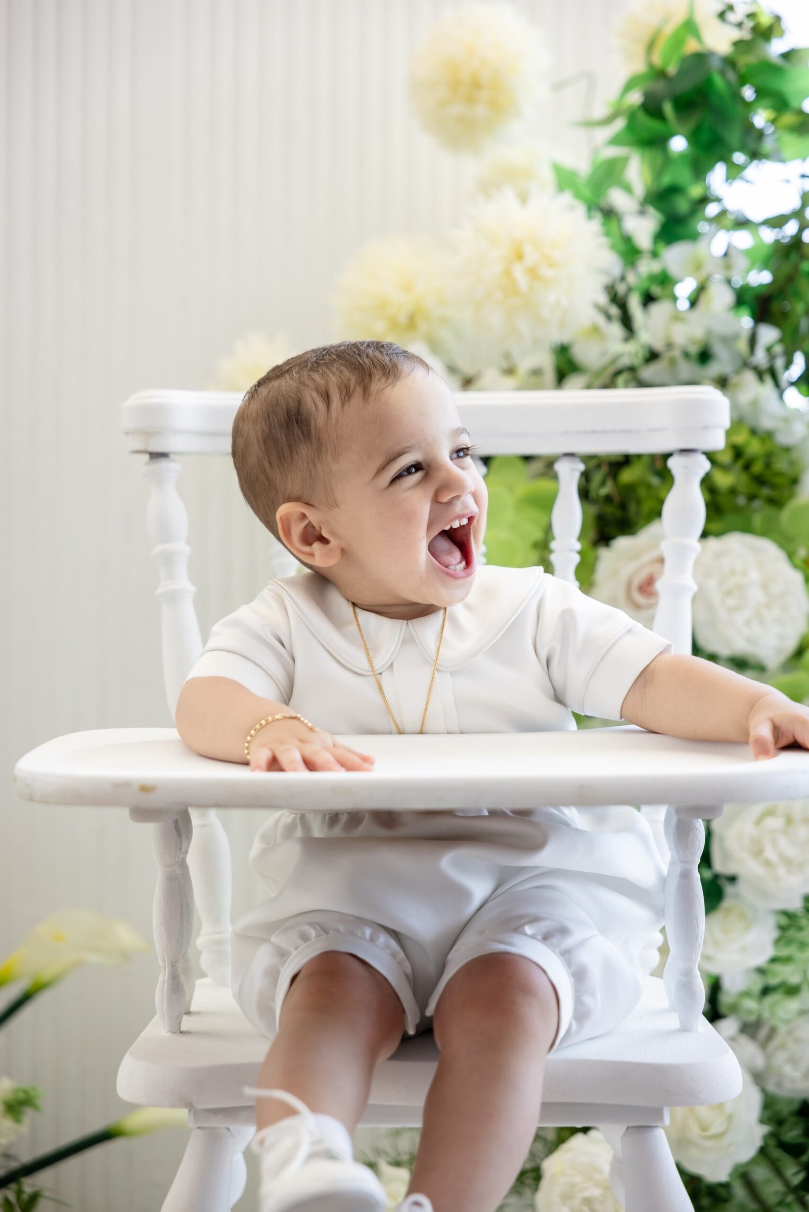 Baby boy laughing in his white christening outfit
